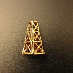 May include: A gold-colored metal charm shaped like an oil derrick. The charm is detailed with a lattice design.