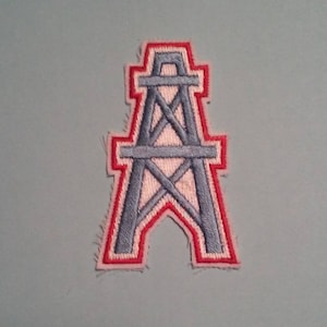 May include: A red and blue embroidered patch featuring an oil derrick, a common symbol for the oil and gas industry.