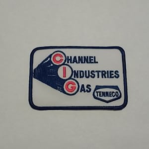 May include: A white rectangular patch with blue edging. The patch features a blue and white logo with the letters "CIG" in red circles. The text "Channel Industries Gas" is written in blue above the logo. The text "Tenneco" is written in blue below the logo.