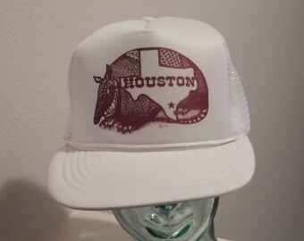 May include: White trucker hat with a red and brown armadillo design and the word "HOUSTON" on the front.