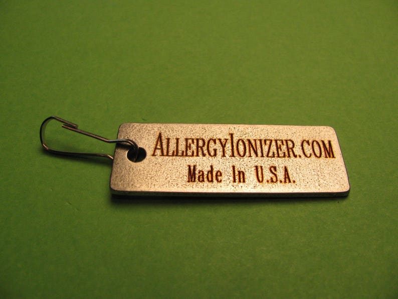 May include: A silver metal tag with a silver metal loop. The tag has the text "ALLERGYIONIZER.COM" and "Made in U.S.A." engraved on it.