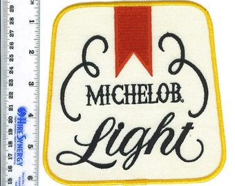 May include: A white embroidered patch with a yellow border. The patch features a red ribbon and the text "MICHELOB Light" in a black cursive font.