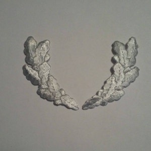 May include: Two white embroidered oak leaf wreaths, each with a curved shape and multiple leaves.