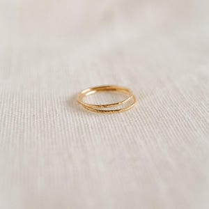 May include: Two thin gold rings stacked on top of each other. The rings have a textured surface.