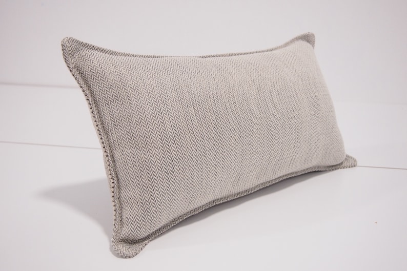 May include: A rectangular throw pillow with a light gray herringbone pattern and a white border.