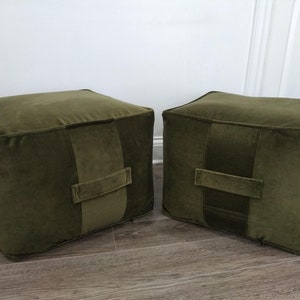 May include: Two green velvet square ottomans with a single stitched seam across the top and a fabric handle on the front.