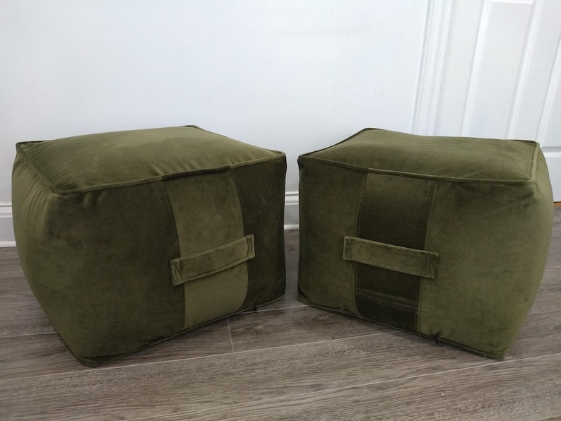 May include: Two green velvet square ottomans with a single stitched seam across the top and a fabric handle on the front.
