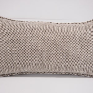 May include: A beige rectangular pillow with a textured fabric. The pillow has a subtle brown pattern and a simple design.