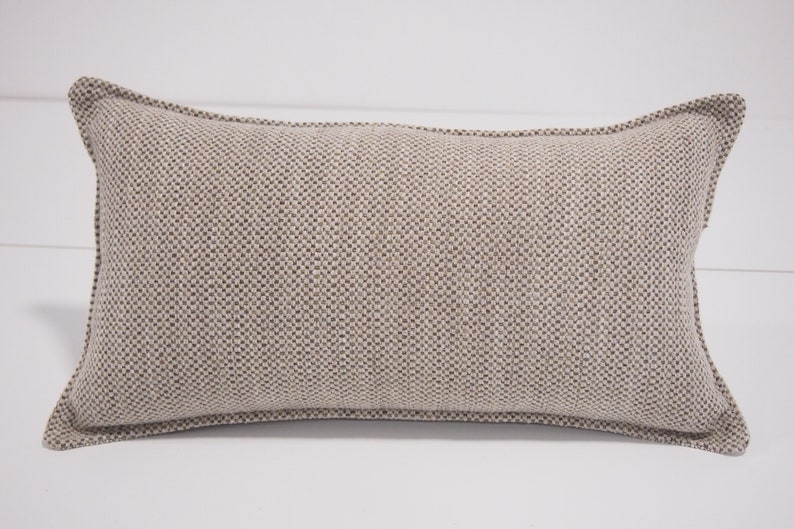 May include: A beige rectangular pillow with a textured fabric. The pillow has a subtle brown pattern and a simple design.