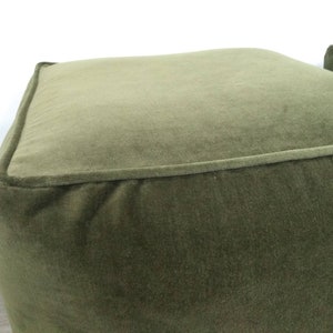 May include: A green velvet ottoman with a square top and a slightly rounded bottom.