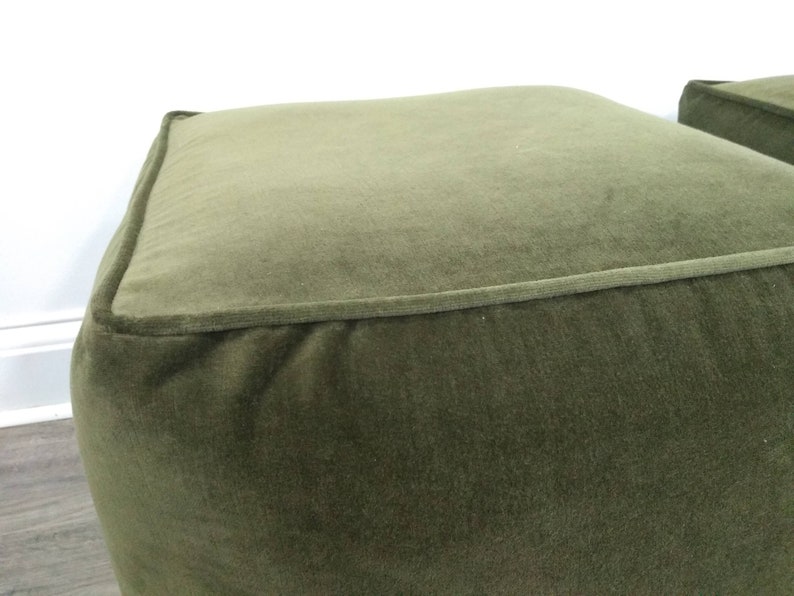 May include: A green velvet ottoman with a square top and a slightly rounded bottom.