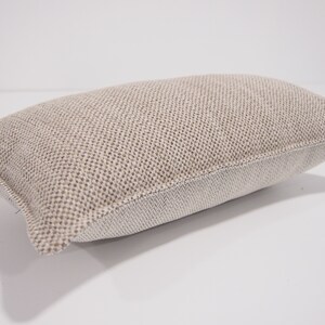 May include: A beige rectangular pillow with a textured woven fabric. The pillow has a white border around the edges.