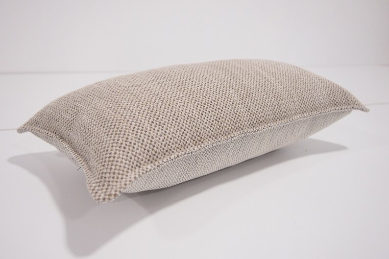 May include: A beige rectangular pillow with a textured woven fabric. The pillow has a white border around the edges.