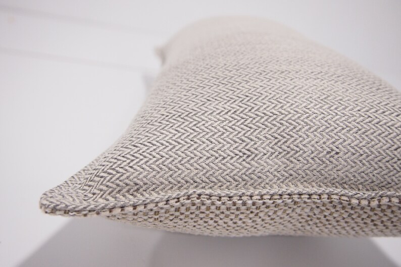 May include: A close-up of a beige pillow with a subtle herringbone pattern. The pillow has a woven edge.