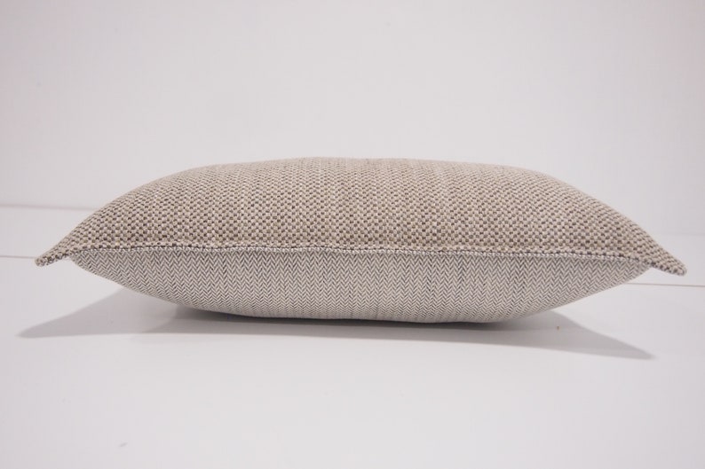 May include: A beige and white rectangular pillow with a textured woven fabric. The pillow has a subtle herringbone pattern on the back.