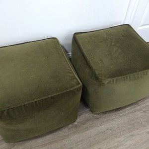 May include: Two square green velvet ottomans. The ottomans are sitting on a wood floor.