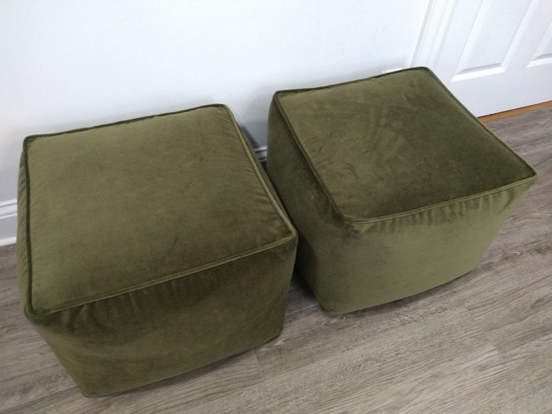 May include: Two square green velvet ottomans. The ottomans are sitting on a wood floor.