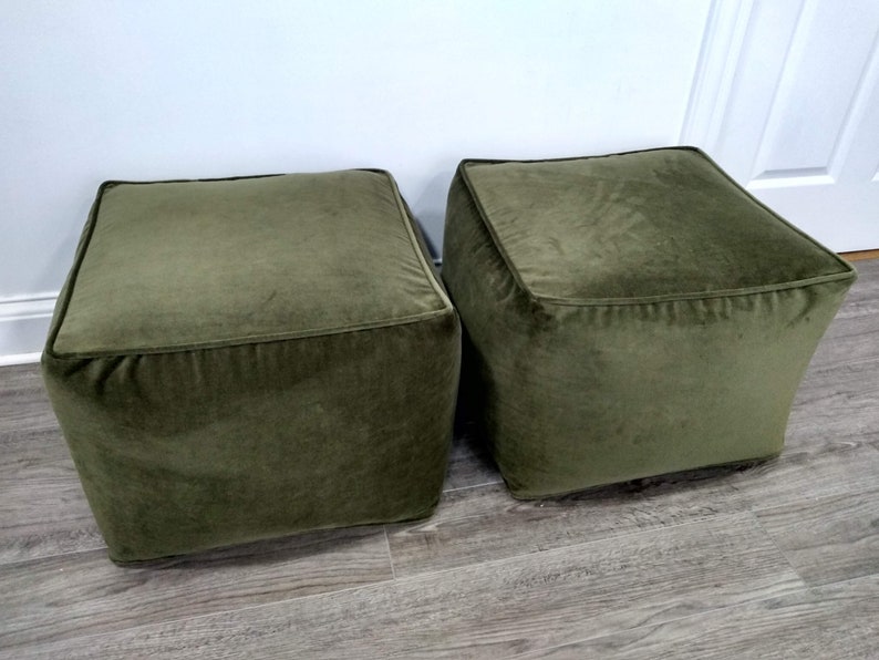 May include: Two square green velvet ottomans. The ottomans are sitting on a wood floor.