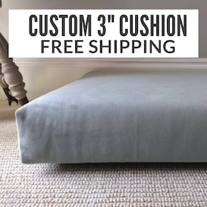 May include: A custom 3-inch cushion in a soft, muted blue-gray fabric. The cushion is rectangular and sits on a neutral-colored carpet. The text "CUSTOM 3" CUSHION" is displayed in bold, black letters.