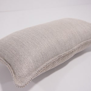 May include: A beige rectangular pillow with a subtle herringbone pattern. The pillow is made of a soft, textured fabric.