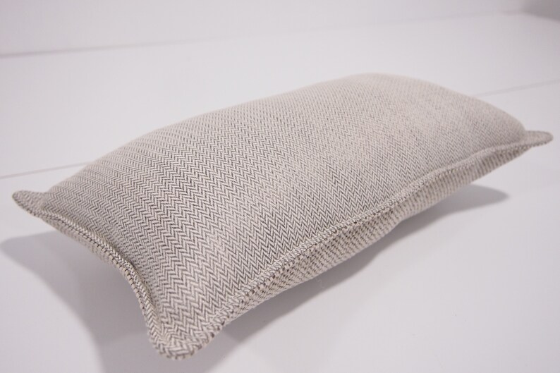 May include: A beige rectangular pillow with a subtle herringbone pattern. The pillow is made of a soft, textured fabric.