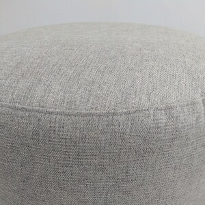K&ouml;nnte beinhalten: Ein grauer Stoffhocker mit einer glatten, strukturierten Oberfl&auml;che.