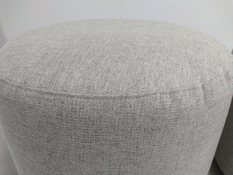 K&ouml;nnte beinhalten: Ein grauer Stoffhocker mit einer glatten, strukturierten Oberfl&auml;che.