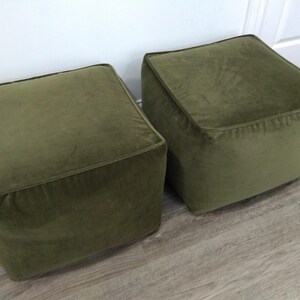 May include: Two square green velvet ottomans. The ottomans are sitting on a wood floor.