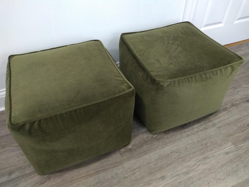 May include: Two square green velvet ottomans. The ottomans are sitting on a wood floor.