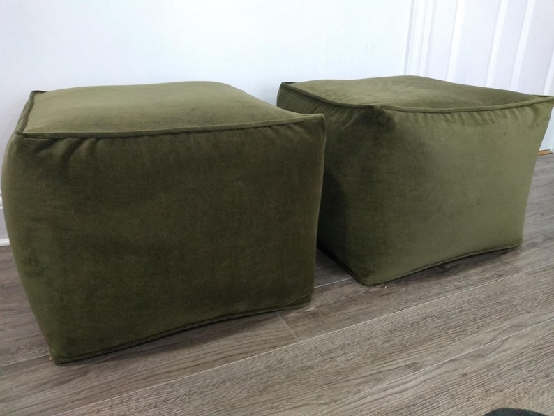 May include: Two square green velvet ottomans. The ottomans are sitting on a wood floor.