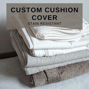 May include: A stack of custom cushion covers in various shades of beige and brown. The top cover is white and the text "CUSTOM CUSHION COVER STAIN RESISTANT" is displayed on a brown background.