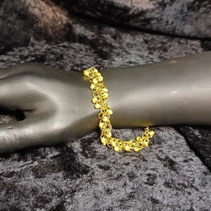 May include: A gold bracelet with a chain made of small, round links. The bracelet is on a black mannequin hand.