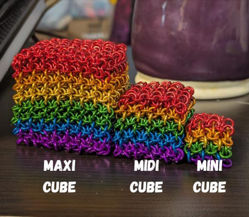 Puede incluir: Tres cubos de cota de malla de colores del arco&iacute;ris en varios tama&ntilde;os: Maxi, Midi y Mini. Los cubos est&aacute;n dispuestos en un degradado de colores, del rojo al morado. El texto "MAXI CUBE", "MIDI CUBE" y "MINI CUBE" est&aacute; debajo de cada cubo.