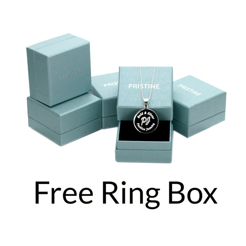 Pode incluir: Uma caixa de anel azul com a palavra "Pristine" impressa nela. A caixa est&aacute; sobre uma superf&iacute;cie branca. O texto "Free Ring Box" est&aacute; impresso abaixo da caixa.
