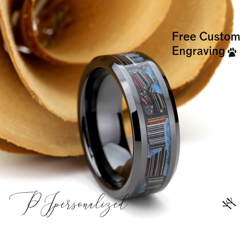 May include: A black ring with a colourful inlay of blue, red, and white materials. The ring has a polished finish and the text "Free Custom Engraving". The ring is set against a neutral background.
