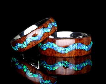 May include: Two wooden rings with a silver band and a blue and green opal inlay. The rings are stacked on top of each other.