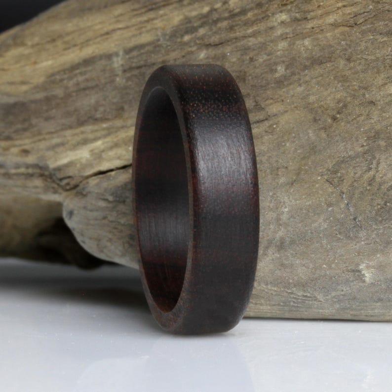 Puede incluir: Un anillo de madera marr&oacute;n oscuro con un acabado liso y pulido. El anillo est&aacute; hecho de madera oscura y tiene un dise&ntilde;o simple y cl&aacute;sico. El anillo mide aproximadamente 1,9 cm de ancho.