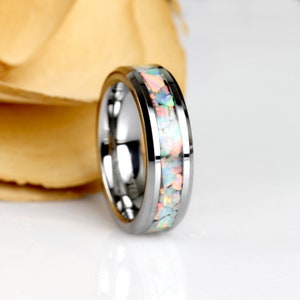 May include: A silver ring featuring a band of colourful opal fragments. The ring has a polished, reflective surface and a central inlay of iridescent opal pieces in white, pink, and green. This ring is a piece of jewellery.