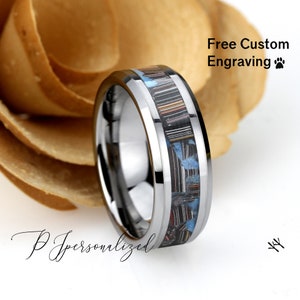 May include: A silver ring with a central inlay of black, blue, and red materials. The ring has a polished finish and a beveled edge. The text "Free Custom Engraving" is visible in the image.