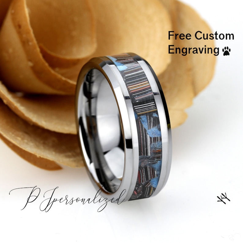 May include: A silver ring with a central inlay of black, blue, and red materials. The ring has a polished finish and a beveled edge. The text "Free Custom Engraving" is visible in the image.
