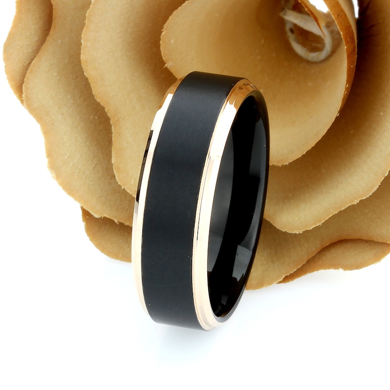 Pode incluir: Um anel de carboneto de tungst&ecirc;nio preto com uma banda de ouro rosa. O anel tem um acabamento escovado e uma borda chanfrada.
