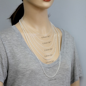 Pu&ograve; includere: Primo piano di un manichino che indossa una camicia grigia e diverse collane a catena d'argento di diverse lunghezze e spessori. Le collane sono etichettate con la loro lunghezza e spessore in millimetri e pollici. 0,9 mm 16", 1,1 mm 18", 1,5 mm 20", 1,8 mm 22", 2,8 mm 24", 3,8 mm 30"