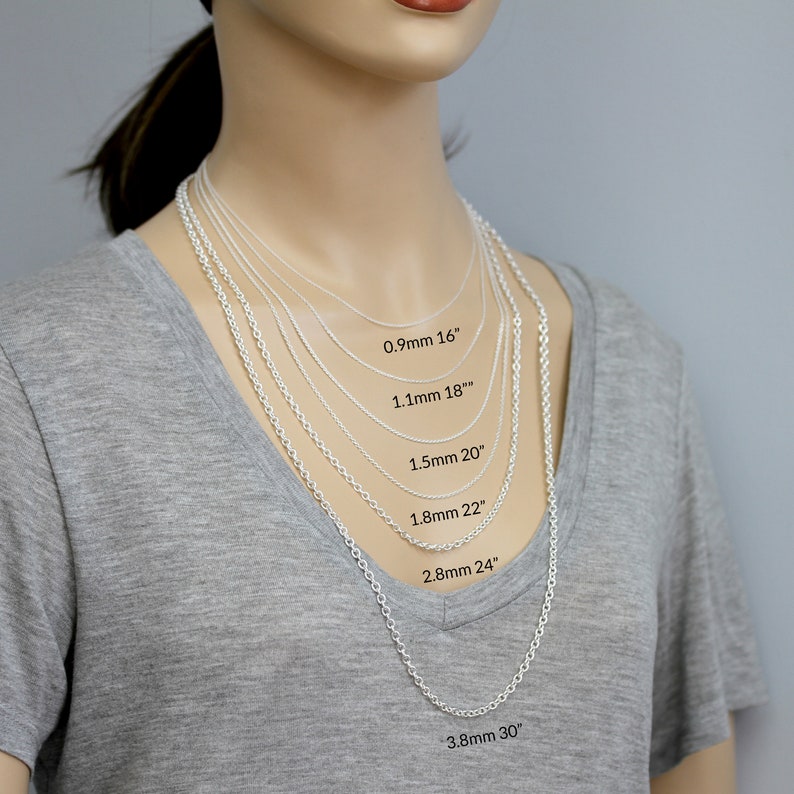 Pu&ograve; includere: Primo piano di un manichino che indossa una camicia grigia e diverse collane a catena d'argento di diverse lunghezze e spessori. Le collane sono etichettate con la loro lunghezza e spessore in millimetri e pollici. 0,9 mm 16", 1,1 mm 18", 1,5 mm 20", 1,8 mm 22", 2,8 mm 24", 3,8 mm 30"