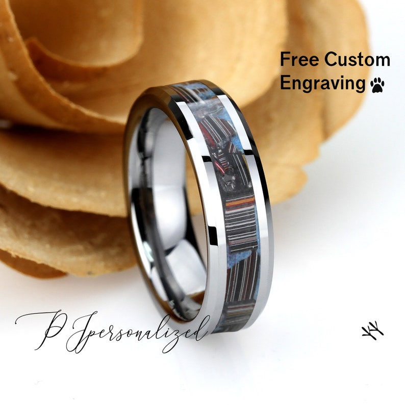 May include: A silver ring with a patterned inlay of red, blue, and black. The ring has a polished finish and the text "Free Custom Engraving". The ring is set against a neutral background.