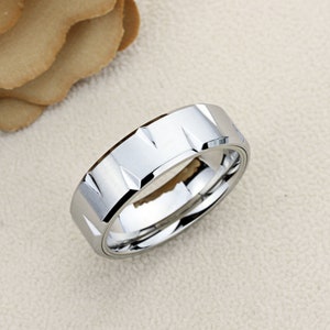 May include: A silver ring with a textured, geometric design. The ring is made of a durable metal and has a polished finish.