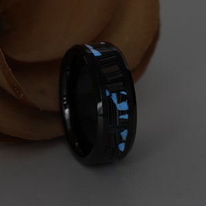 May include: A black ring with a textured inlay and bright blue accents. The ring has a polished finish and a modern design. The blue accents are scattered across the band, creating a unique pattern.