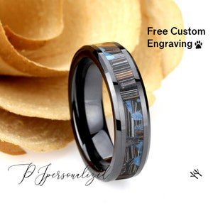 May include: A black ring with a patterned inlay of blue, brown, and white. The ring has a polished finish and the text "Free Custom Engraving". The ring is displayed against a neutral background.