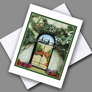 May include: A vintage postcard featuring a black wrought iron gate with a decorative arched top and a white background. The gate is surrounded by lush green vines and flowers in shades of red, pink, and white.