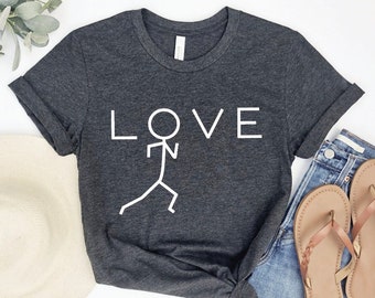 May include: Dark gray t-shirt with the word "LOVE" in white block letters and a stick figure graphic. The shirt is paired with denim shorts and sandals. The shirt is made of a soft material.
