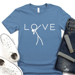 May include: A blue t-shirt with the word "LOVE" printed in white, with a stick figure holding a ball in the middle of the word. The stick figure is doing a dance move.